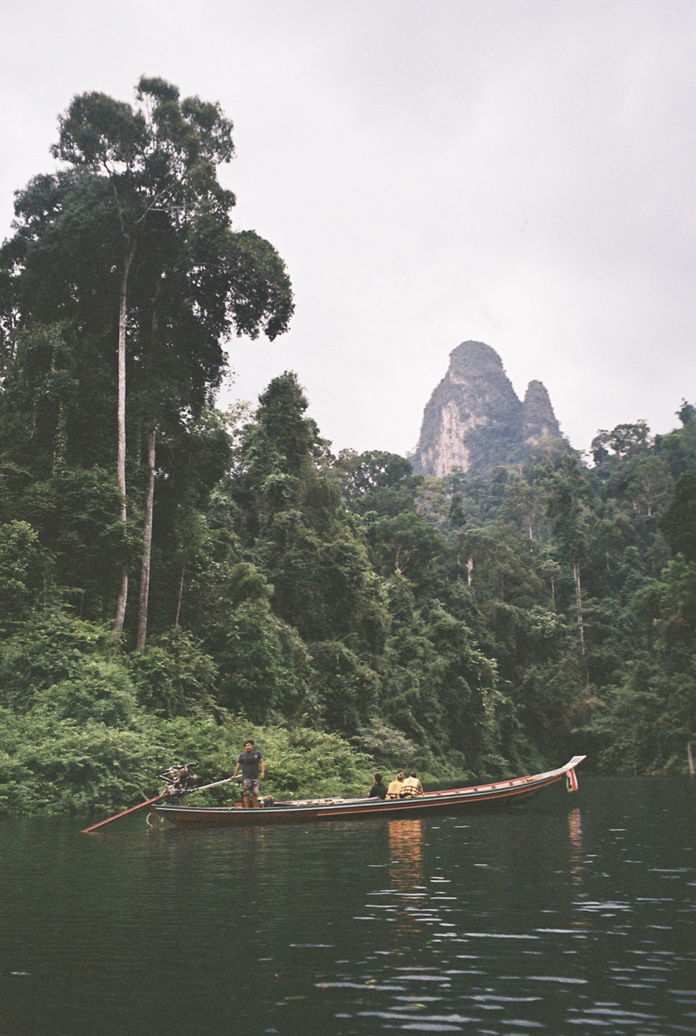 A longtail boat on an emerald lake below a karst peak