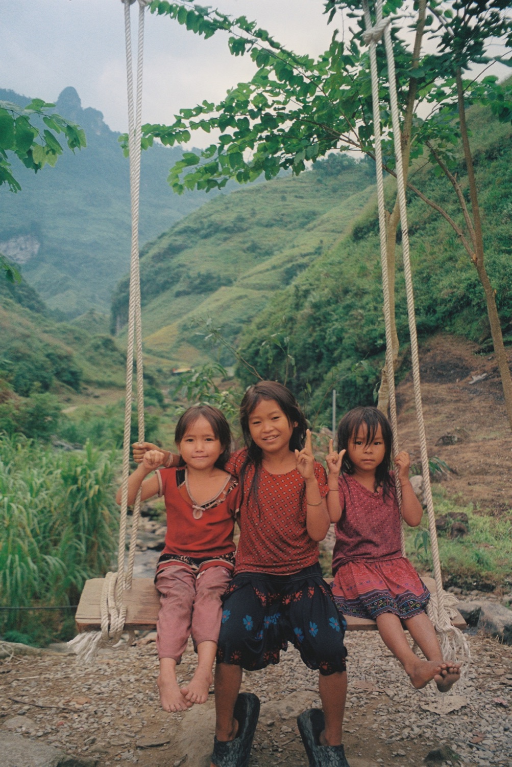 Three children on a swing above green mountains