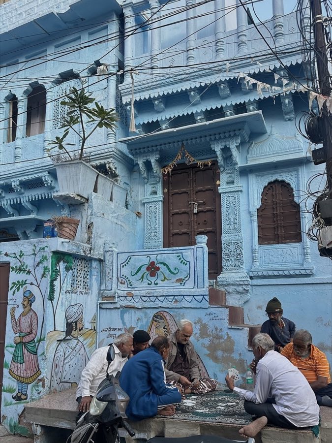 Men playing a game in a lane below a painted blue haveli