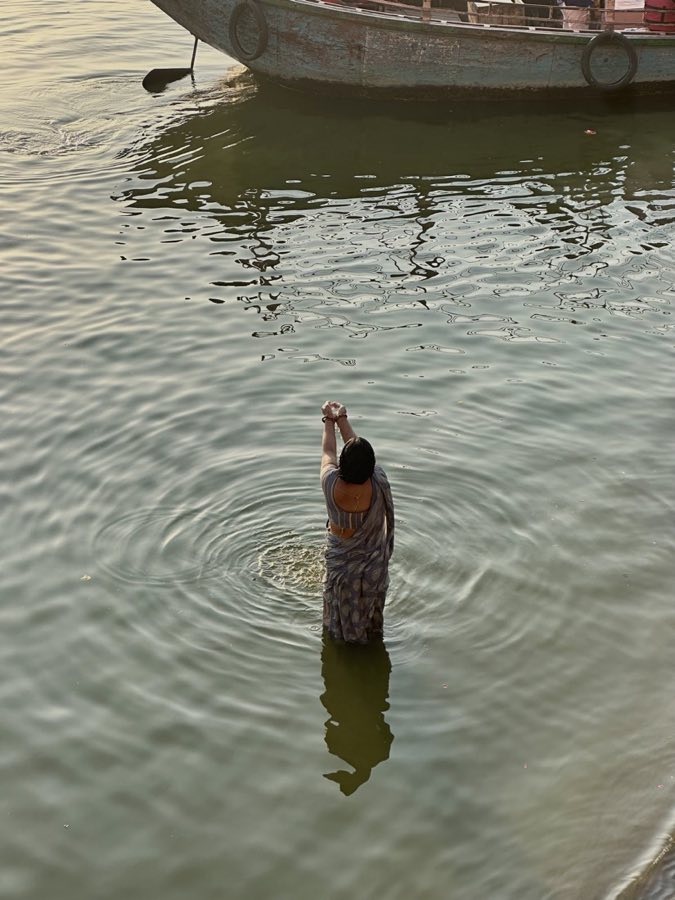 A woman offering water to the Ganges at dawn, ripples around her