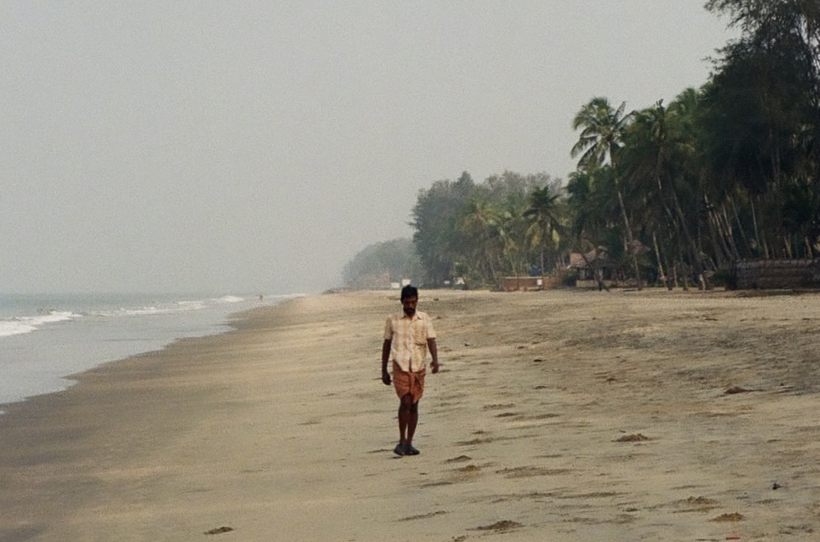 A man walking toward the camera along the beach