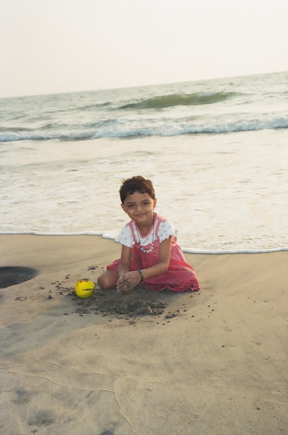 A girl playing on the sand with a yellow ball